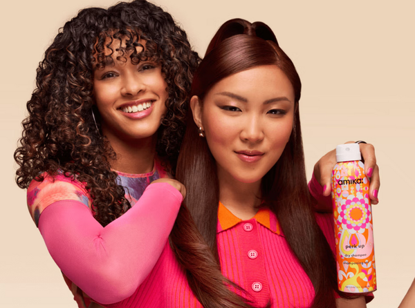 Two women in brightly coloured clothing with different hair textures, one of them holding an Amika product
