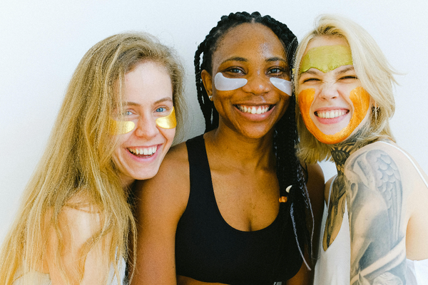 three women wearing under eye patches and face masks smiling at the camera