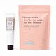 Frank Body exfoliator set featuring a white tube of lip balm with a black cap next to a large peach-pink stand-up pouch of Original Coffee Scrub, on a white background.