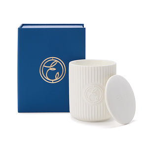 White ceramic candle with lid and blue packaging box featuring a logo on a white background