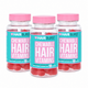 Three clear plastic bottles of Hairburst Chewable Hair Vitamins with bright pink caps and turquoise labels, arranged in a clean studio shot on a white background.