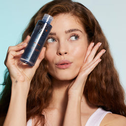 a model holding the bottle of cleanser to her face