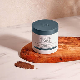Christophe Robin Cleansing Thickening Paste With Tahitian Algae texture next to the tub placed on a wooden slab