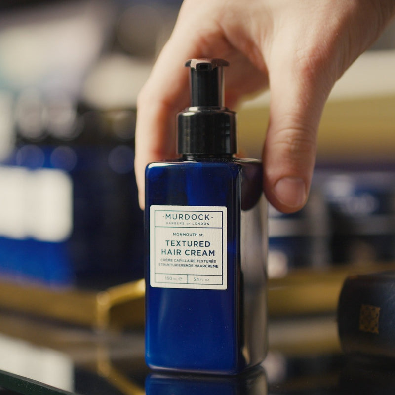 a hand places the Murdock London Textured Hair Cream bottle on a glass surface