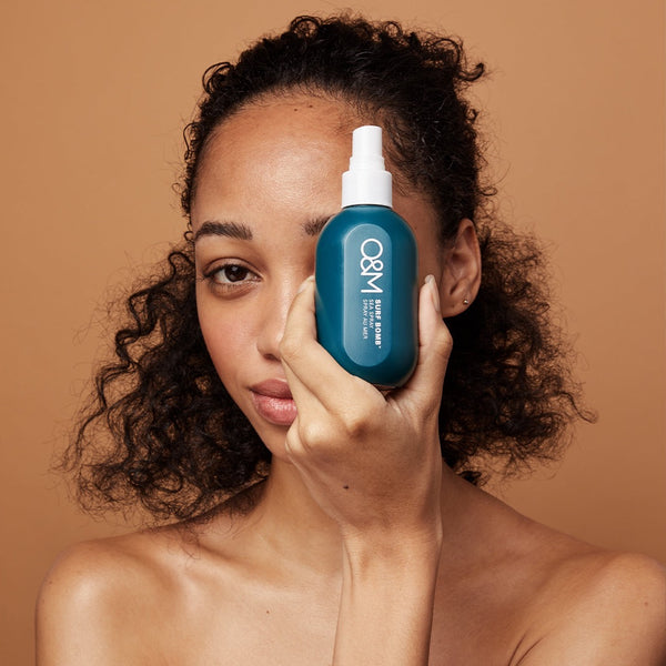 model holding a bottle of O&M Surf Bomb in front of her face