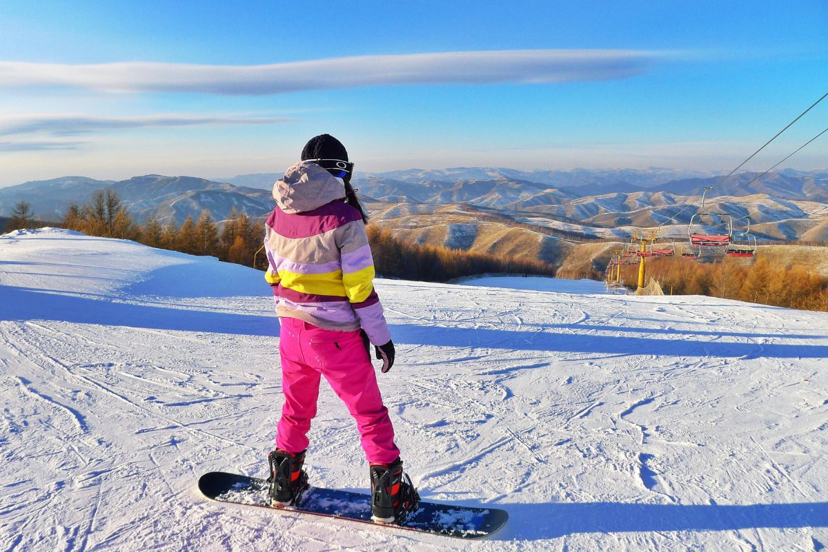 woman in colourful snow suit on a snowboard looking over the slopes