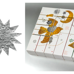 A white advent calendar box with illustrated gold and silver bird, crescent moon, and star designs, shown next to a close-up of a textured silver star embellishment on a light gray background.