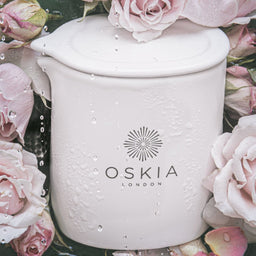 OSKIA Rose De Mai Massage Candle surrounded by flowers