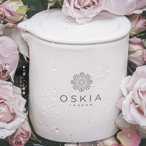 OSKIA Rose De Mai Massage Candle surrounded by flowers