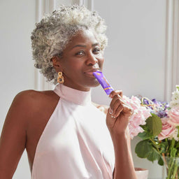 Woman holding a purple product with flowers in the background