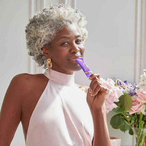 Woman holding a purple product with flowers in the background