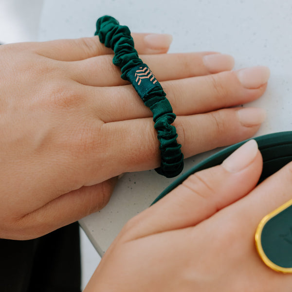 A close-up of a dark green elastic bracelet with a gold chevron pattern, worn on a person's hand.