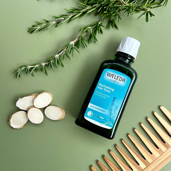 Weleda bottle with rosemary branch, roots, and wooden comb on a green background