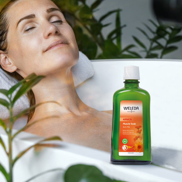 Woman relaxing with a towel on her head, Weleda bottle in the foreground, surrounded by greenery.