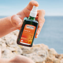 Person holding a Weleda massage oil bottle with a scenic background