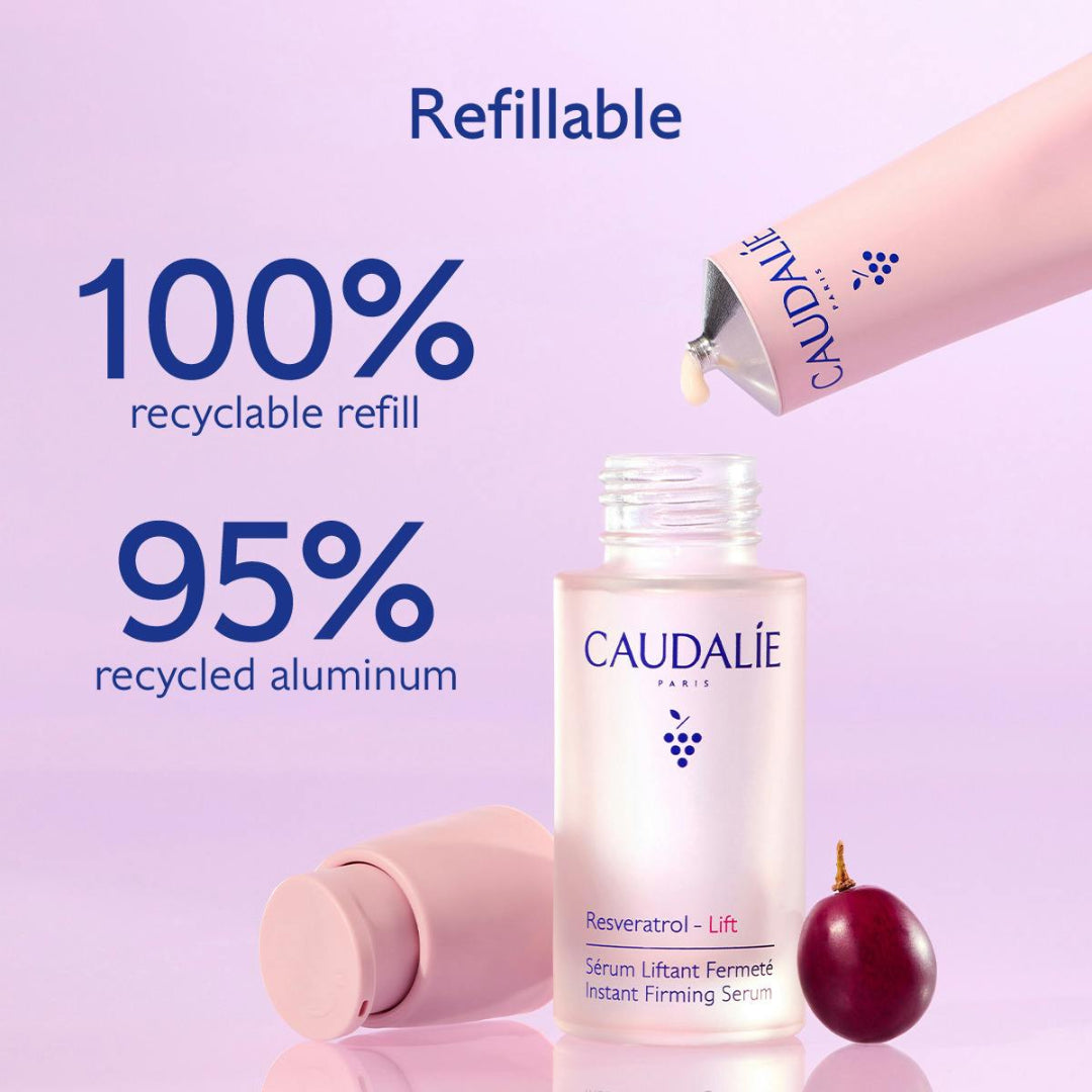 Caudalé Paris refillable serum bottle shown with a pink applicator tube being dispensed, a second tube lying on its side, and a small red fruit on a soft lavender background. Large text highlights recyclable refill and recycled aluminum.