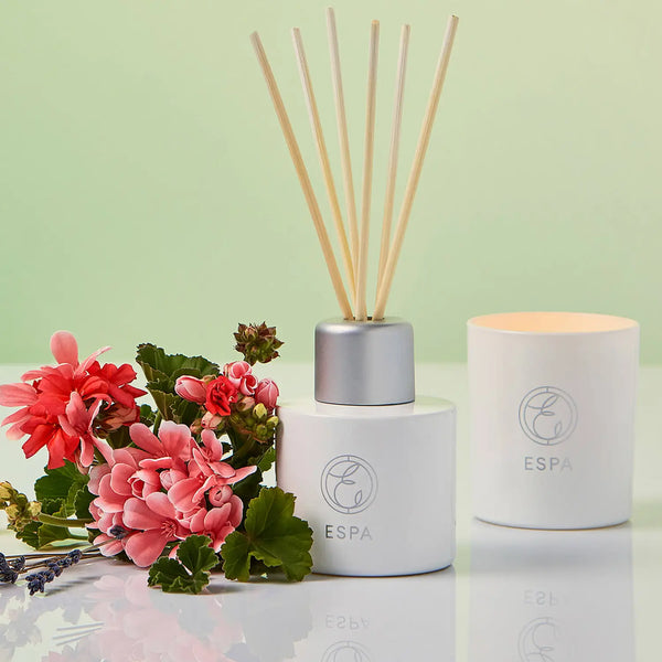 ESPA Restorative Reed Diffuser next to a lit candle and a bunch of flowers