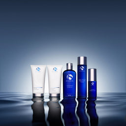 A five-piece skincare set from AEGENAL, including white tubes and blue bottles with silver caps, arranged on a reflective dark blue surface against a dark blue gradient background.