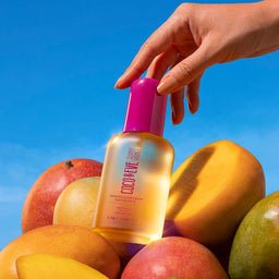 Coco & Eve Sunny Honey Tan Boosting Anti-ageing Body Oil SPF30 in front of a mango pile
