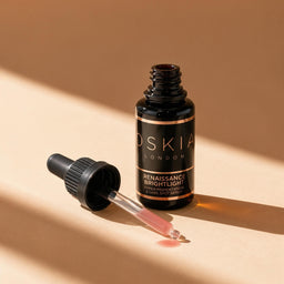 A bottle of Roséé London Renaissance Brightlight serum with its dropper removed and placed beside it on a warm beige background with strong diagonal shadows.