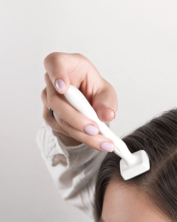 Hand using a white hair removal tool on a person's head against a light background