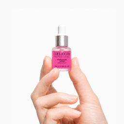 Hand holding a pink serum bottle with a white cap on a light gray background