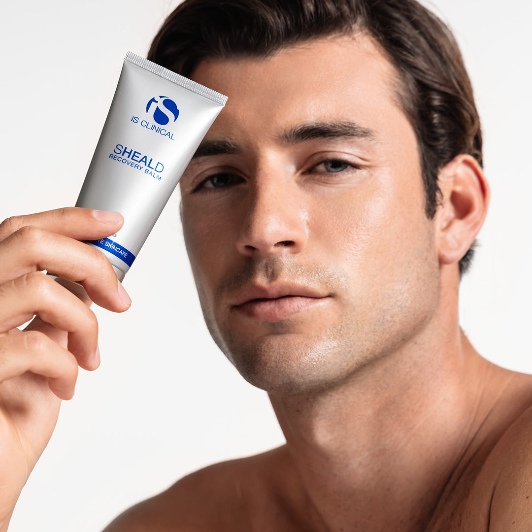 Man holding a tube of IS Clinical SHEALD Recovery Cream against a white background