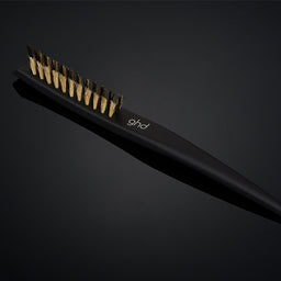 Black hair straightening brush with gold accents on a dark background