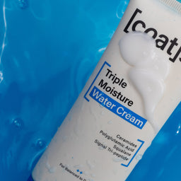 A white tube of Coat's Triple Moisture Water Cream with blue accents, partially submerged in bright blue water with ripples and droplets.
