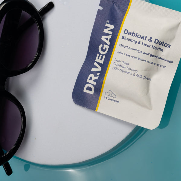 A Dr. Vegan Debloat & Detox blister pack lies on a white circular tray next to black sunglasses, set against a bright turquoise background.