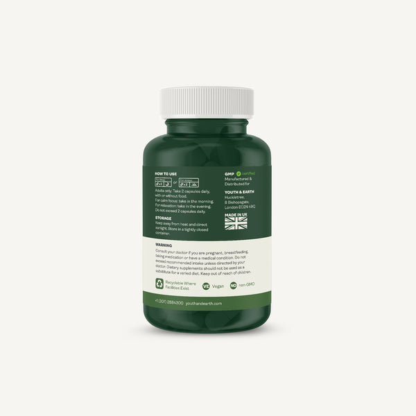 A dark green supplement bottle with a white cap, showing the back label with text, icons, and a small Union Jack, on a light gray background.
