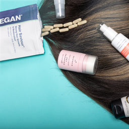 Hair care products on a turquoise background with hair strands.