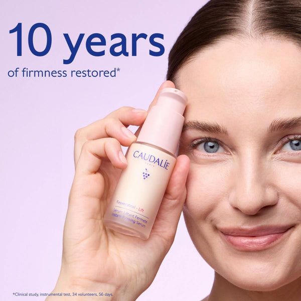 A woman holds a bottle of Caudalie Effacer Lines Visibles Retinol Night Repair Lotion against a light lavender background, with text reading '10 years of firmness restored'.