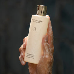 Hand holding a Revitalash bottle against a dark background