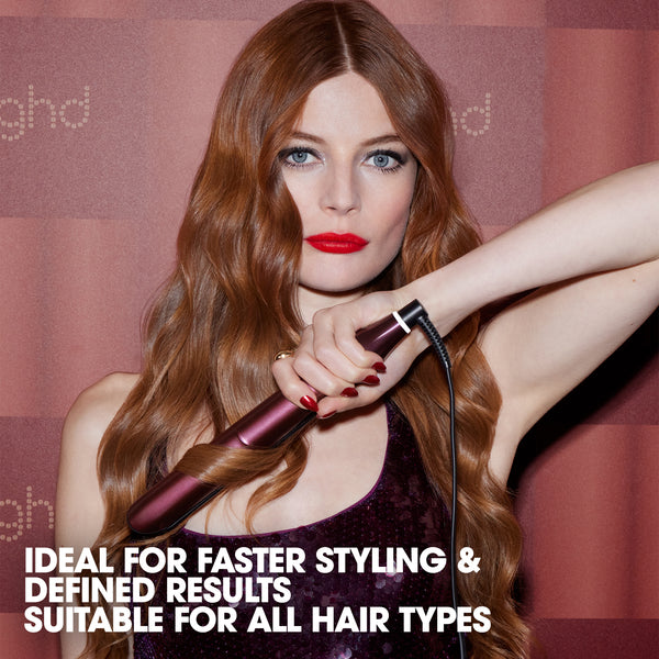 Woman with long hair holding a hair styling tool against a branded background