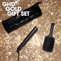 GHD Gold gift set with hair straightener, brush, and pouch on a glittery background