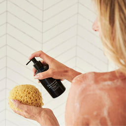 a women applying Olverum Body Cleanser to a sponge in the shower