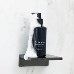 a bottle of Olverum Body Cleanser covered in soap on a shower stand