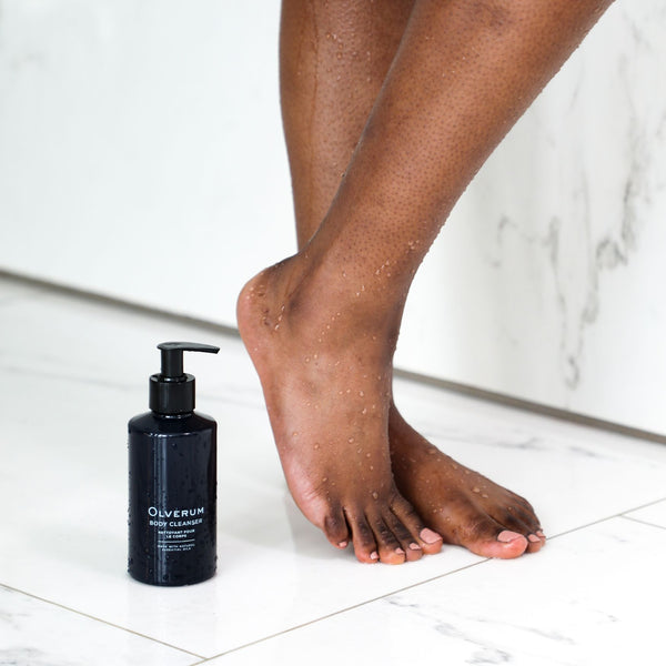 a bottle of Olverum Body Cleanser next to a person stood in the shower