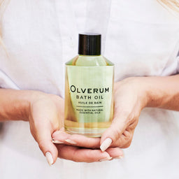 a bottle of Olverum Bath Oil held close to a persons chest