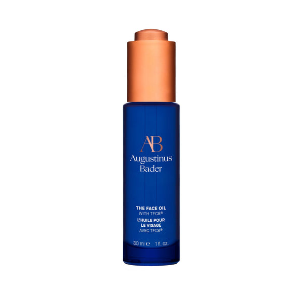 Blue bottle of Augustinus Bader face oil with a copper cap on a white background