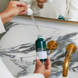Person holding a dropper bottle labeled 'Density' over a marble sink.