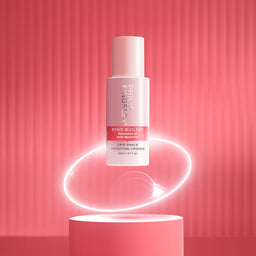 Philippines Bond Builder Lip Shield Protection Lipgloss in a frosted white bottle with pink accents, floating above a pink pedestal against a pink ribbed background with a glowing ring effect.