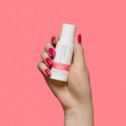 A hand with bright pink manicured nails holds a white bottle of Philip Ketsing Bond Builder Bond Enhancing Treatment against a solid pink background.