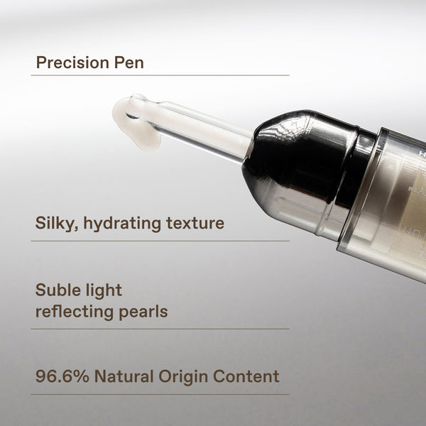 Close-up of a cosmetic applicator pen with a clear tip and black cap, shown on a light gray background with descriptive text callouts about precision, silky hydrating texture, subtle light reflecting pearls, and 96.6% natural origin content.