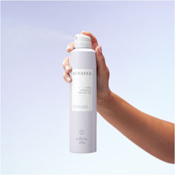 Hand holding a KERASILK product against a light purple background