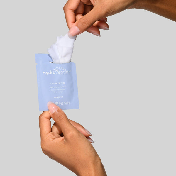 Hand holding a skincare product package with a gray background