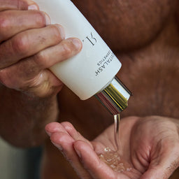 Person pouring a clear liquid from a white bottle into their palm.
