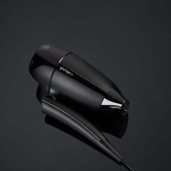 Black hair dryer on a reflective black surface with a dark background