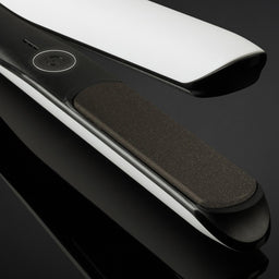 Black and silver hair straightener on a reflective black surface